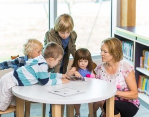 Teacher With Students Using Digital Tablets In Library